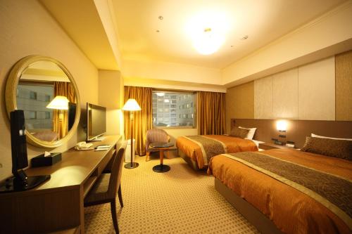 長野市にあるホテルメトロポリタン長野のベッド2台、デスク、鏡が備わる客室です。