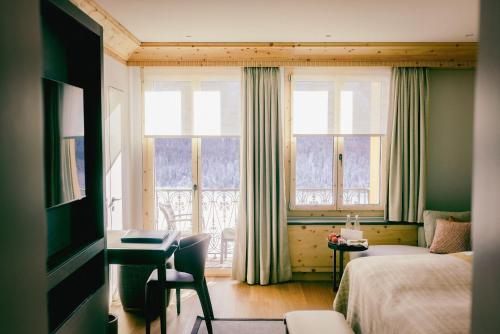 a bedroom with a bed and a desk and a window at Kulm Hotel St. Moritz in St. Moritz