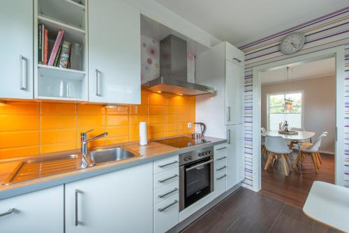 a kitchen with white cabinets and an orange tile wall at Ferienhaus Witt in Neue Tiefe Fehmarn