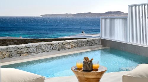 a swimming pool with a table with two glasses of orange juice at Etere Luxury Suites in Agios Ioannis Mykonos