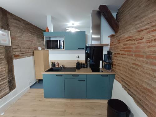 une cuisine avec des placards bleus et un mur en briques dans l'établissement Studio typique Albigeois - quartier calme, à Lescure-dʼAlbigeois
