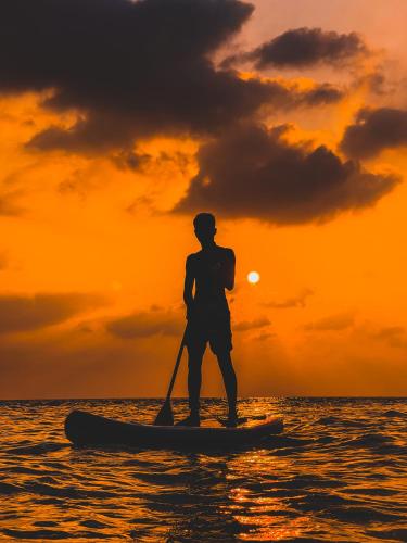 a man standing on a paddle board in the ocean at sunset at Shadow Isles Himandhoo in Himandhoo 