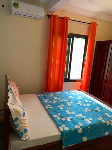 a bed in a room with orange curtains and a window at Résidence Yavanie in Kribi