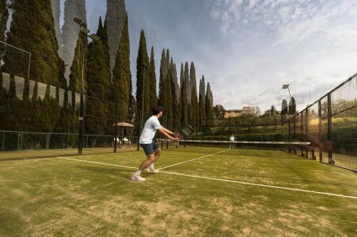 a man holding a tennis racket on a tennis court at COMO Castello Del Nero in Tavarnelle in Val di Pesa