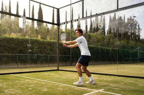 a man holding a tennis racket on a tennis court at COMO Castello Del Nero in Tavarnelle in Val di Pesa