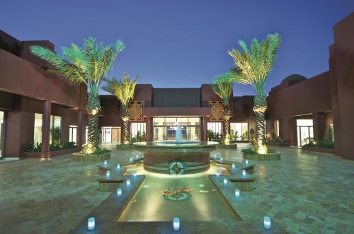 a courtyard with a fountain and palm trees in front of a building at Mövenpick Resort & Spa Tala Bay Aqaba in Aqaba