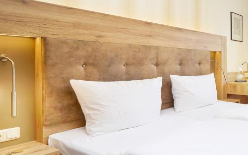 a bed with white pillows and a wooden headboard at Strandhotel garni Kormoran in Zinnowitz