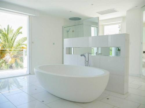 La salle de bains blanche est pourvue d'une grande baignoire et d'une fenêtre. dans l'établissement EDEN ROC Luxurious villa with sea view & huge pool in Cap d'Antibes, à Antibes
