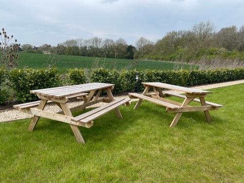 two wooden picnic tables sitting on the grass at Rose Garden lodge stunning views in Turvey