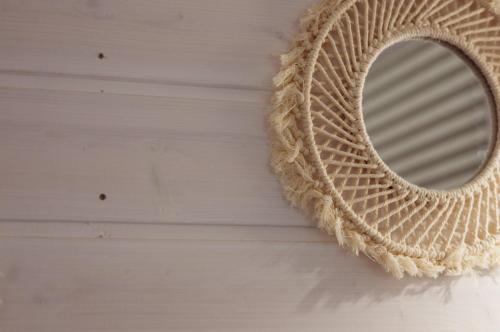 a rattan mirror hanging on a white wall at Tajnikowo Sekretny Tiny House Anyżek in Łubiana