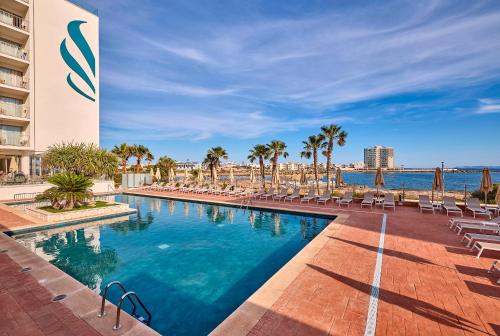 a swimming pool with chairs and the ocean in the background at Universal Hotel Romantica in Colonia Sant Jordi