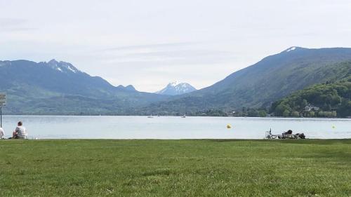 deux personnes assises sur l'herbe près d'un lac avec des montagnes dans l'établissement Maison détente, à Cuincy