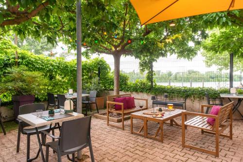 a patio with tables and chairs and an umbrella at Kyriad Hotel Lyon Givors in Givors