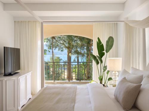 a bedroom with a white bed and a balcony at Grecotel Eva Palace in Kommeno