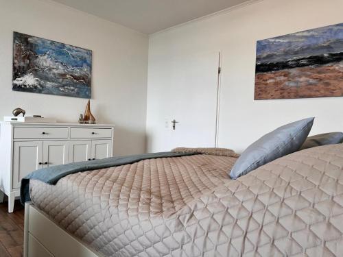a white bedroom with a bed and paintings on the wall at Baltic Sea View in Fehmarn