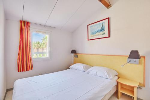 Un dormitorio con una cama blanca y una ventana. en Résidence Odalys Le Grand Bleu, en Vendres-Plage