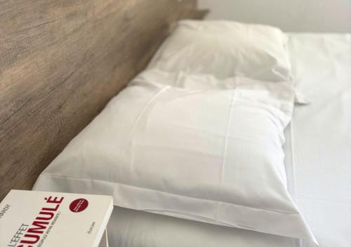 a bed with white sheets and a book on it at Hôtel Le Carnon in Carnon-Plage