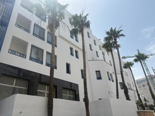 a white building with palm trees in front of it at Hôtel Fnideq Senator in Fnidek