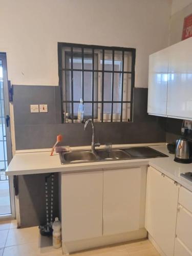 a kitchen with white cabinets and a sink and a window at Travellers Ensuites, La Beach Hub in Trofwi