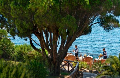 a man standing next to a tree next to the water at Luna Sardinia in Santa Margherita di Pula