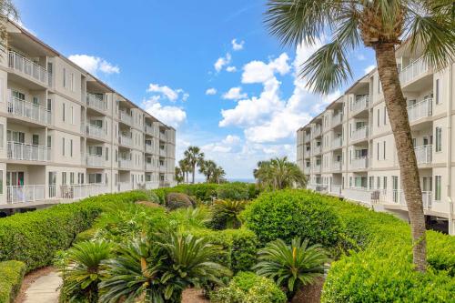 an apartment building with a palm tree and bushes at Sail Inn SaintSimons-ground unit beach access pool in East End