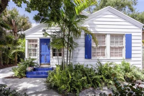 a white house with blue doors and a palm tree at Palm Beach Oasis - Indulge in Garden Tranquility with Alfresco Dining in West Palm Beach
