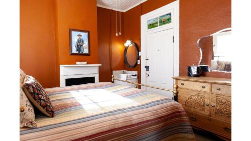 a bedroom with orange walls and a bed and a dresser at Doc Holiday - Historic Hotel in Cimarron