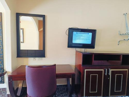 a room with a desk with a television and a mirror at Capital O Deluxe Inn Channelview Houston I-10 in Channelview