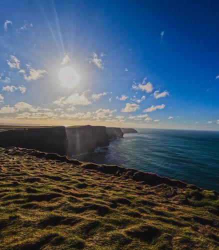 a view of the ocean from a beach with the sun at Coach House Lodge in Lahinch