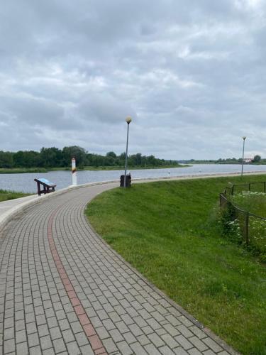 a brick walkway next to a lake with a bench at Apartamentai Rusnėje, žvejų ir paukščių rojuje in Rusnė