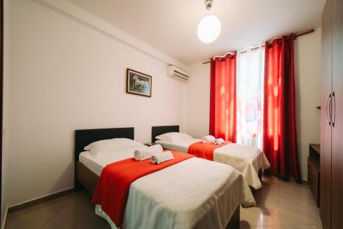 two beds in a room with red curtains at Hotel Skrapari in Çorovodë