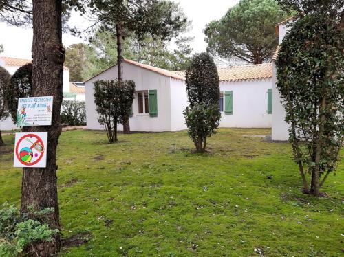 un bâtiment blanc avec des arbres et un panneau dans une cour dans l'établissement Vacation home in a wooded park, à Saint-Jean-de-Monts