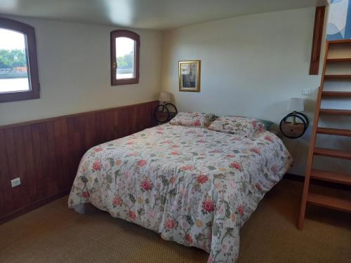 a bedroom with a bed with a floral bedspread and two windows at Péniche UHARTEA chambre d'hôtes "Baionako Gambara" in Bayonne