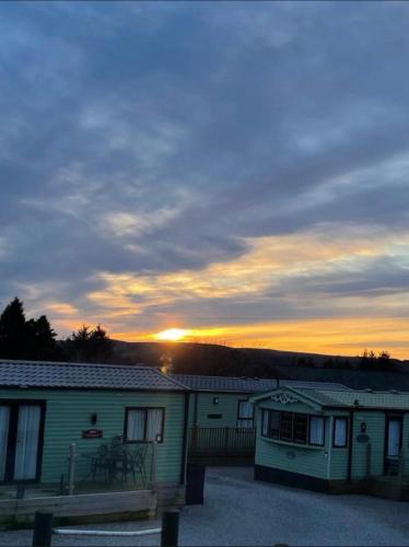 a sunset behind two buildings with a bench in front at West Lakes Affordable Caravan in Lamplugh