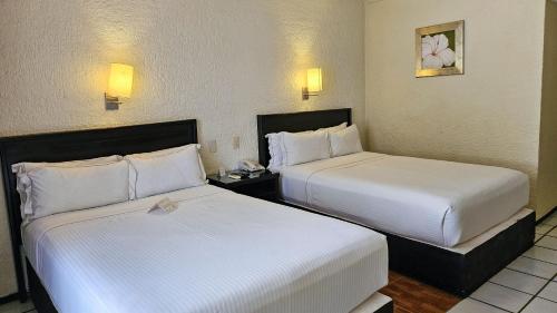 two beds in a hotel room with white sheets at Casa Francisco in Cuernavaca