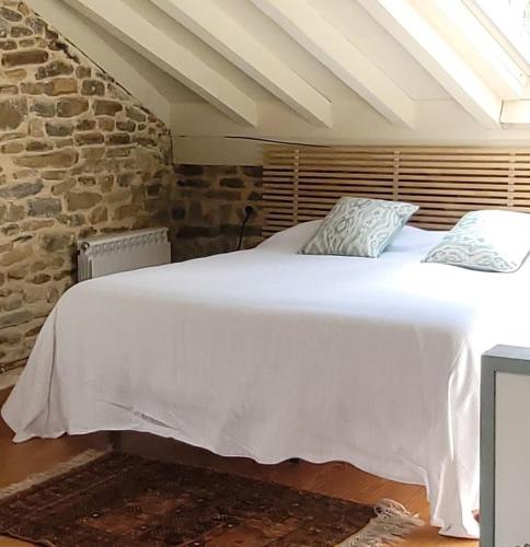 a bedroom with a white bed with a stone wall at La cabaña de San Pelayo in San Pelayo