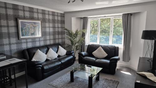 a living room with black leather furniture and a window at Levenhowe Holiday Apartment in Balloch