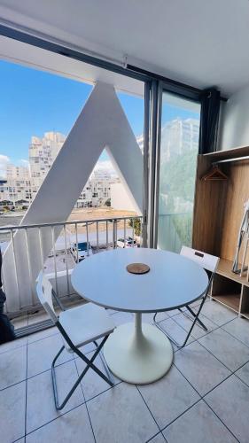 - une table et des chaises blanches dans une chambre dotée d'une grande fenêtre dans l'établissement La Cachette 70 et 139, à La Grande Motte