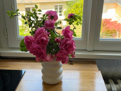 un vase blanc rempli de fleurs roses sur une table dans l'établissement Villa Auguste chambre lumineuse, à Quimper