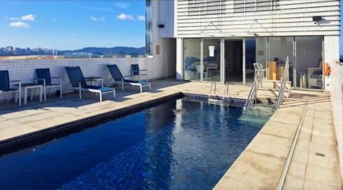 a swimming pool in front of a house with chairs and tables at Apartamento Santos praia Helbor Stay in Santos