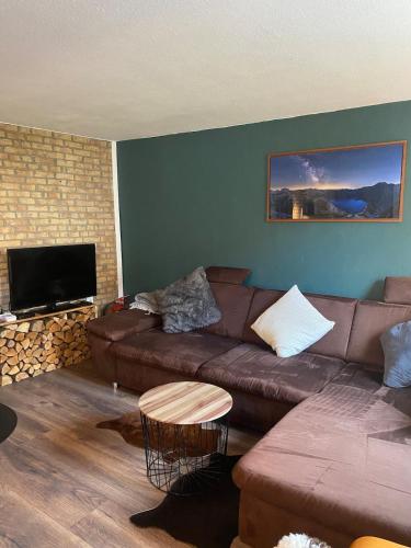 ein Wohnzimmer mit einem braunen Sofa und einem TV in der Unterkunft FERIENHAUS ZUM BULLERJAN - Coozy Haus mit Kamin in EuÃŸerthal