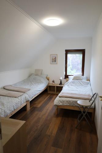 two beds in a room with wooden floors and a window at Hamvas Vendégház Tiszakécske in Tiszakécske