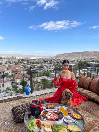 een vrouw in een rode jurk zittend naast een tafel met eten bij Goreme Palace Cave Suites in Goreme