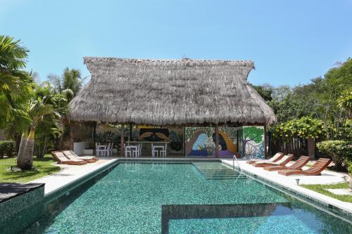 a resort swimming pool with chairs and a thatch roof at Villas H2O in Tulum