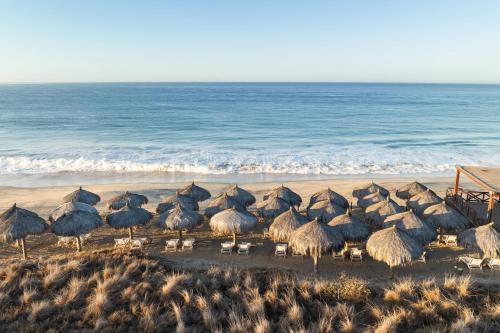 a group of straw umbrellas and chairs on a beach at Secrets Puerto Los Cabos Golf & Spa18+ in San José del Cabo
