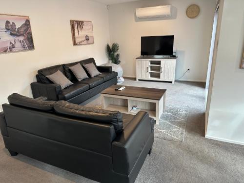 a living room with a black couch and a tv at Airport Retreat 4 Bedrooms 8 Guests in Christchurch