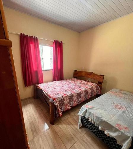 a bedroom with two beds and a window with red curtains at Chacara Linhares in Pirenópolis