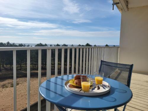 une table bleue avec une assiette de nourriture et deux verres de jus d'orange dans l'établissement Appartement rénové pour 4 pers., vue mer, salle de jeux et parking inclus - FR-1-364-180, à Saint-Brévin-les-Pins