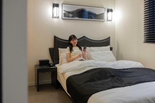 a woman sitting on a bed reading a book at Aank Hotel and Spa Daejeon Yuseong in Daejeon