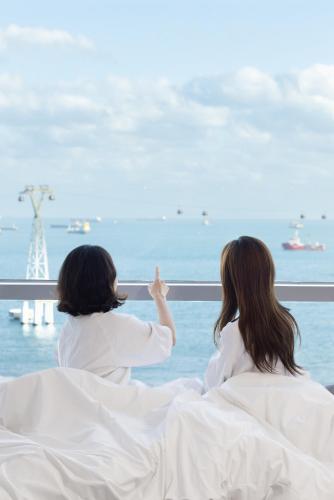 two women sitting in bed looking out at the ocean at Fairfield by Marriott Busan Songdo Beach in Busan